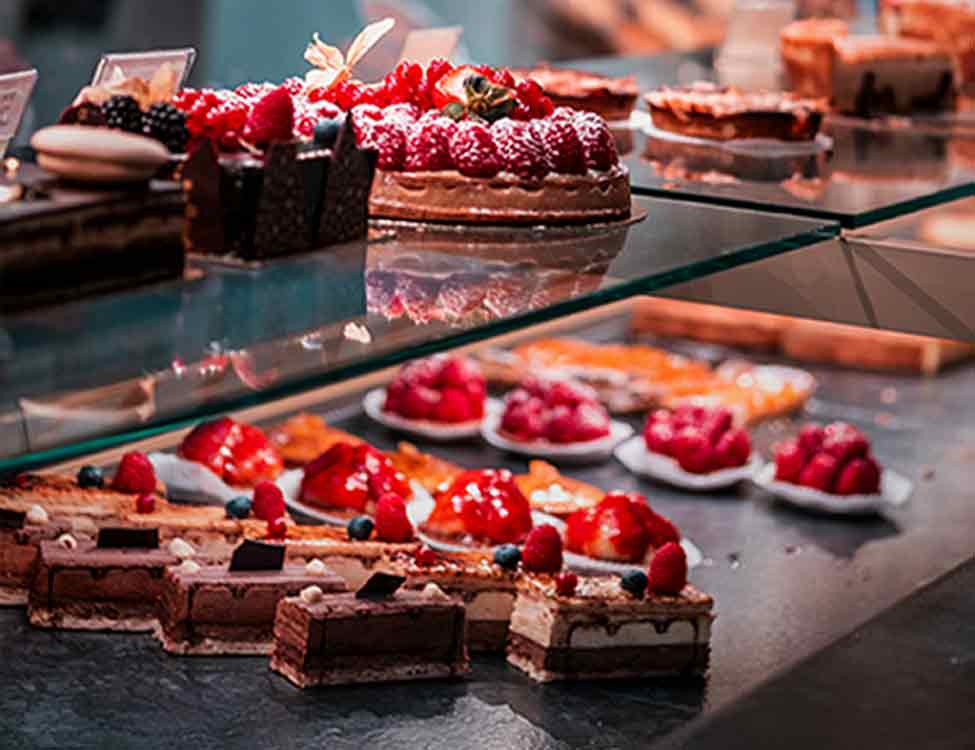 strawberry cakes, cupcakes and chocolate slice cakes in a glass display case